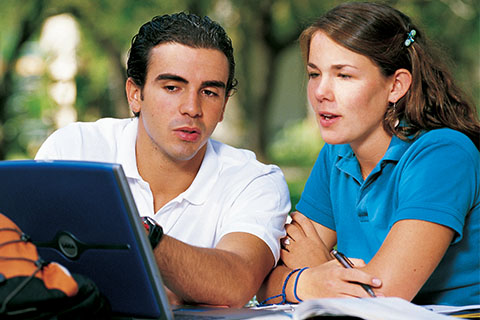 Two students sitting outside and discussing an assignment on their computer