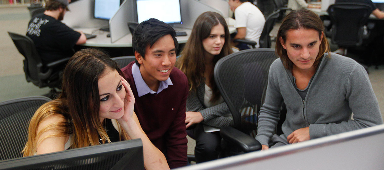 Four students sit around a computer in the Richter Library